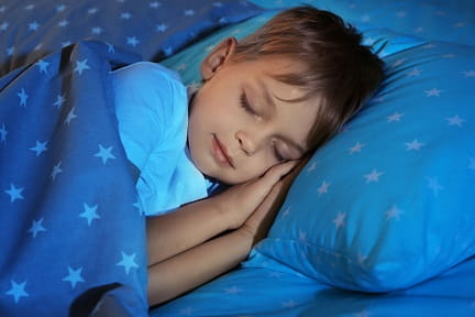Young boy sleeping on a blue bedspread with stars