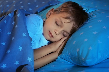 Young boy sleeping on a blue bedspread with stars