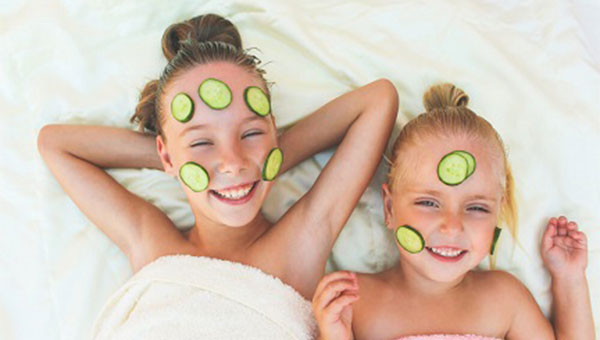 Two young girls, who have cucumber slices on their faces, are enjoying time at a spa.