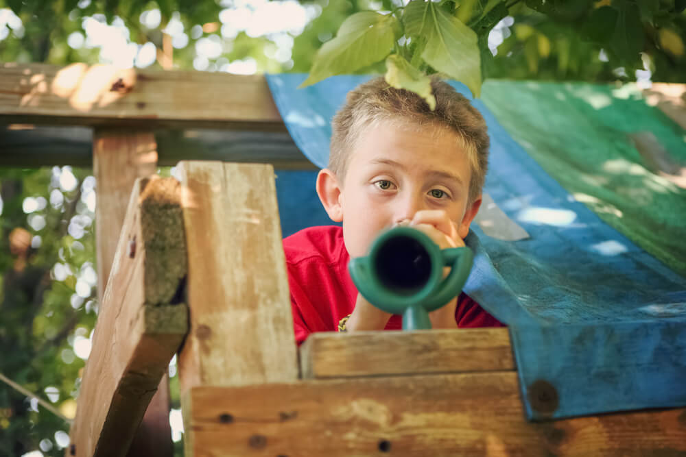boy in a tree house using a toy telescope