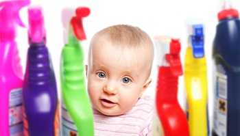 A baby is looking at a cabinet full of household cleaning bottles.