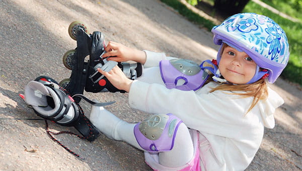Little girl is putting on her rollerblades with a helmet and kneepads on on