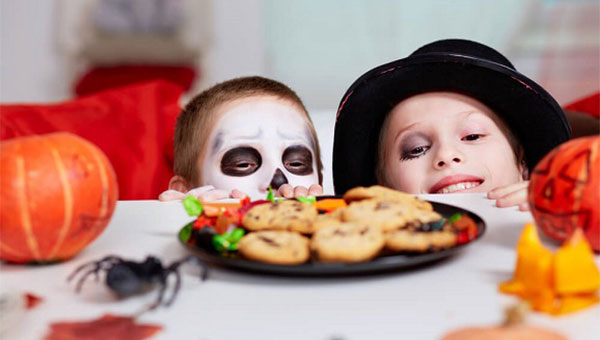 Two costumed kids are looking at a plate of cookies.
