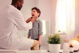 male doctor examining the tonsils of a male child