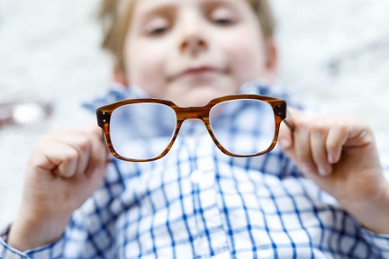A boy is holding his eyeglasses.