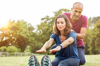 man and woman in a park helping each other stretch 