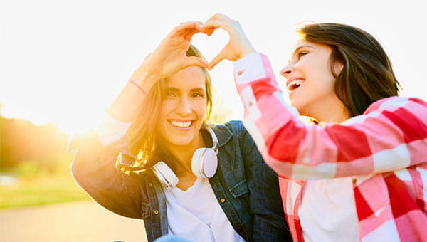 Two female friends use their hands to form the shape of a heart.