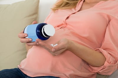 A pregnant woman is pouring prenatal pills into her hand
