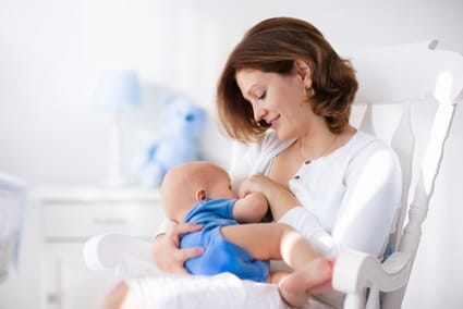 A mom sits in a rocking chair while breastfeeding her baby.