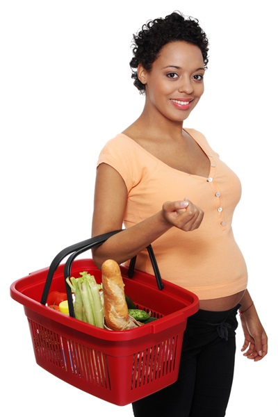 A pregnant woman is carrying a shopping basket filled with healthy foods.