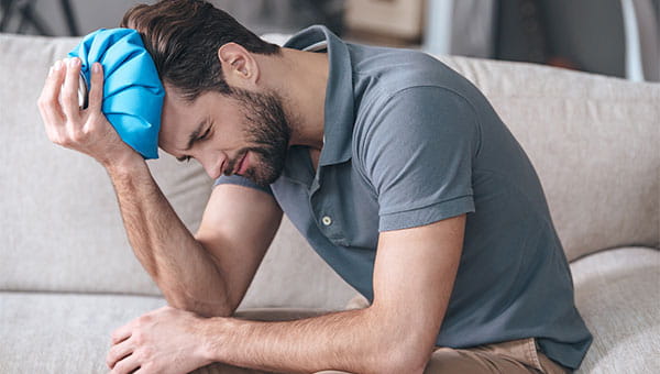 A young man is in pain and is holding an ice pack on his head.