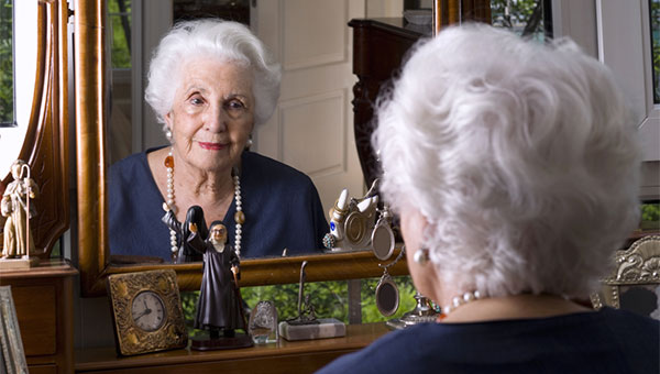 A senior woman is looking at herself in a mirror.