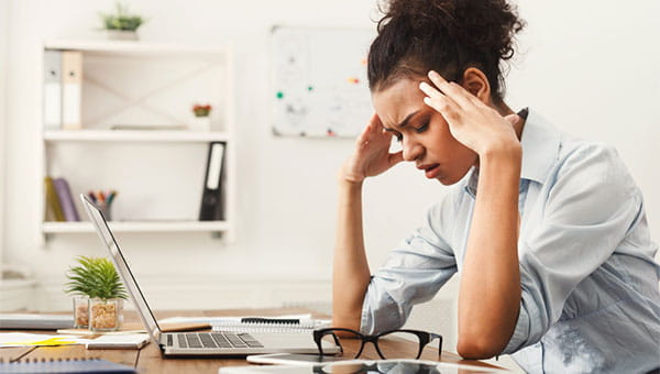 A young woman is having a migraine headache and is resting her head on her hands.