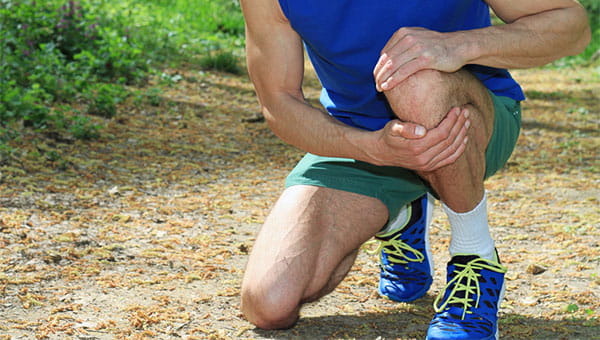 A man is in pain. He has stopped running and is holding onto his left knee.