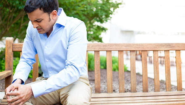 A young man is in pain and is sitting on a bench, holding his knee.