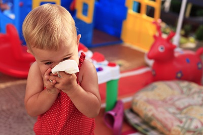 A toddler uses a tissue to wipe her nose.