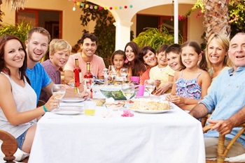 Several generations of a large family is sitting outdoors and enjoying a meal together.
