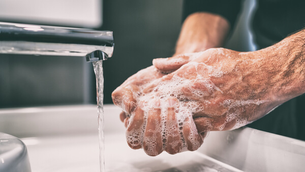 Male washing hands with soap and water in white sink