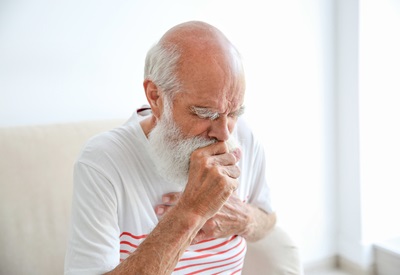 A senior man is coughing while holding his chest.