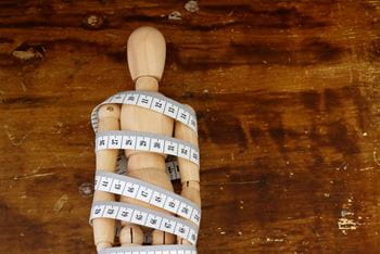 Ball-jointed doll wrapped with tape measure on wooden background