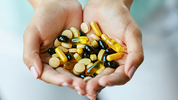 A woman is holding several vitamin and supplement pills in her hands.