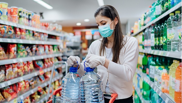 woman wearing mask and gloves adding water jugs to her shopping cart