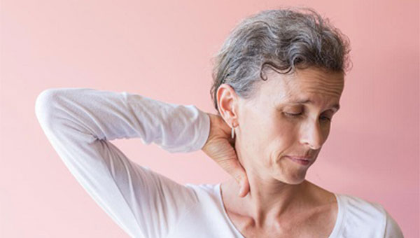 An older woman is rubbing the back of her neck.
