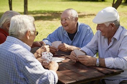 A group of older friends is playing cards in the park.