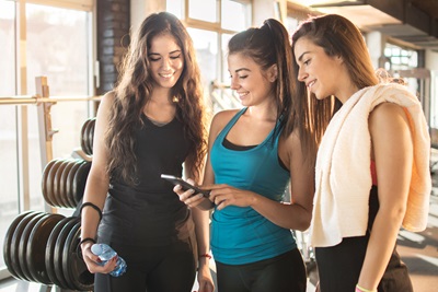 Three young women check a health app after working out at the gym.