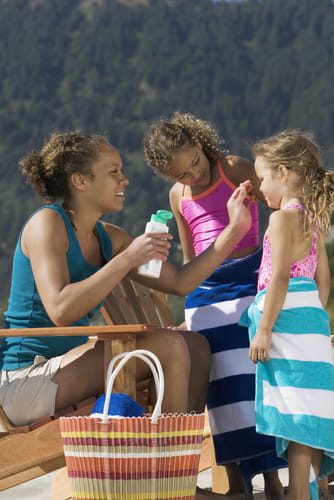 A woman puts sunscreen on her two young daughters.