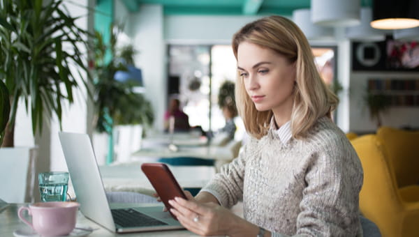 A woman is using her mobile phone and laptop.