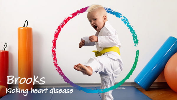 A 5-year-old child with a yellow karate belt performing a karate kick in a fitness area, showing a focused karate kicking expression. The photo has words that say, Brooks, kicking heart disease.