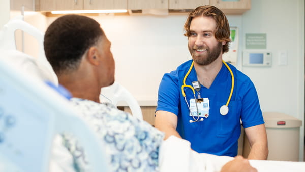 Student Rotations at BayCare Male BayCare team member smiling at a patient in a hospital room.