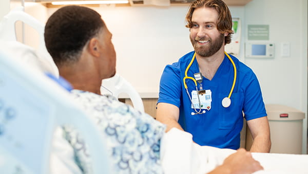 young male baycare clinician wearing blue scrubs and assisting his patient