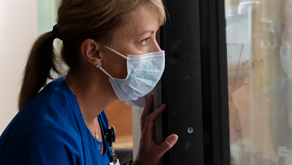 a woman wearing a facemask looking through a window at the covid ward