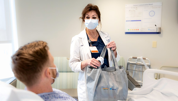 a woman with a mask holding a bag full of food in a patients room
