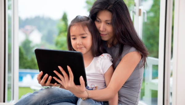 A child sitting on her mothers lap in front of a tablet device.