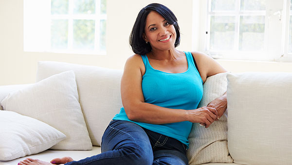 A smiling woman is relaxing on her sofa.