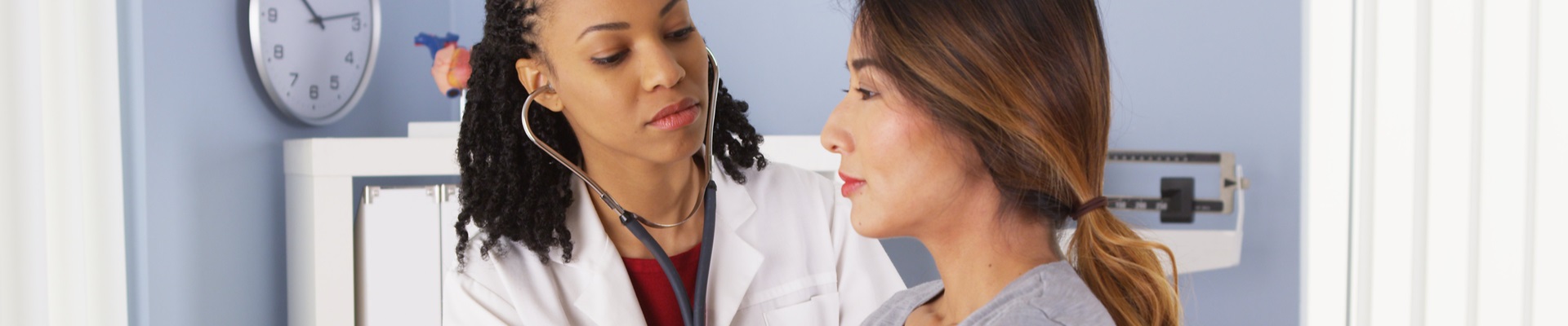female physician holding stethoscope to her female patient