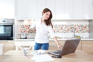 Woman cooking in kitchen while looking at a laptop