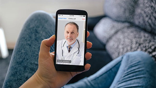 A person is at home on the sofa and using a cellphone for an online doctor visit.