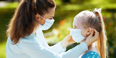 A mom is wearing a mask while putting a mask on her daughter's face.