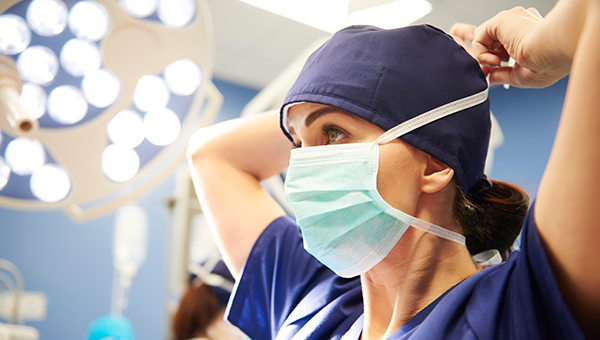 Female medical provider in blue scrub top putting on a face mask