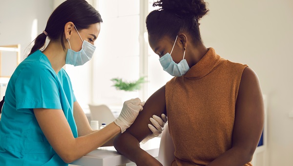 A nurse is wearing a mask while vaccinating a woman who is wearing a mask.