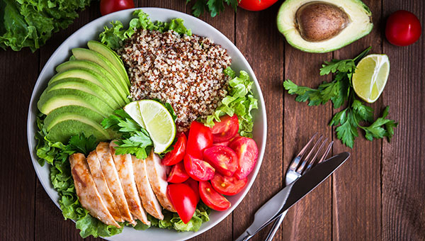 bowl of food with chicken, grains, avocado and tomatoes with knife and for on the side