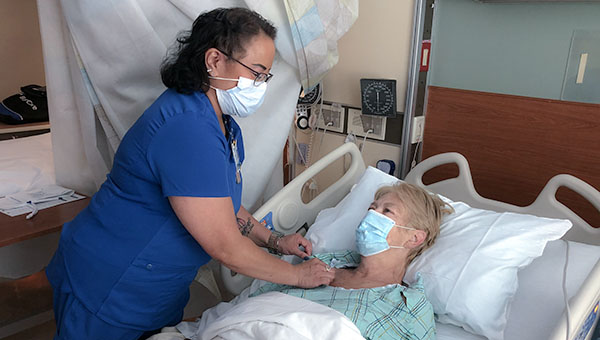 nurse helping a patient who is in a hospital bed.