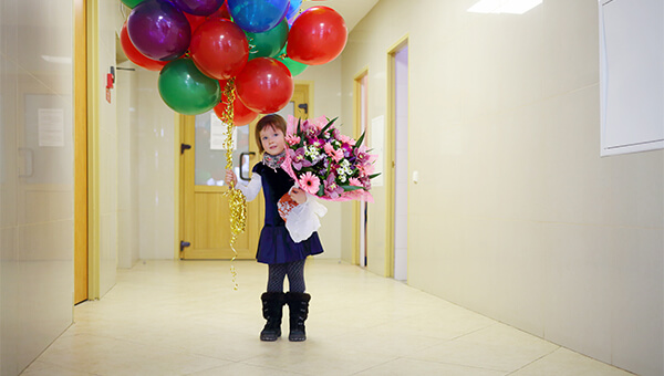 A girl holding balloons and flowers in a hospital hallway
