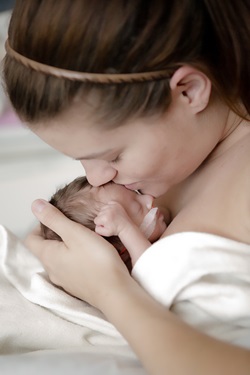 A mother is kissing the forehead of her newborn baby.