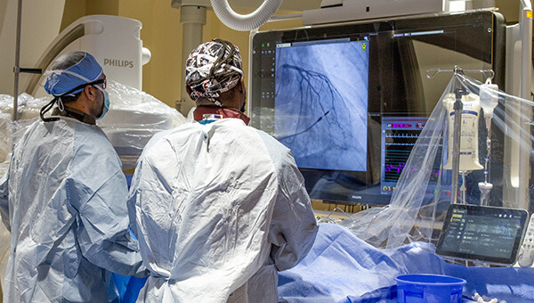 Medical staff in surgical garb viewing an image on a large screen