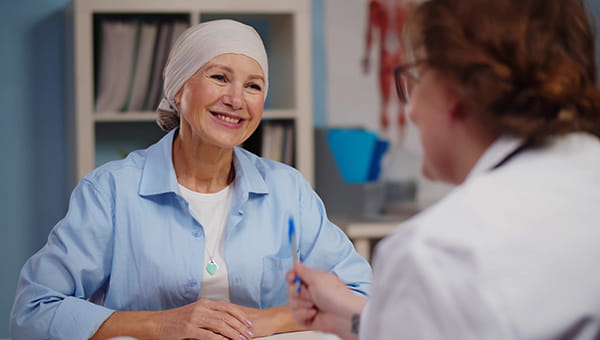 A female cancer patient  converses with a doctor in a clinical setting.